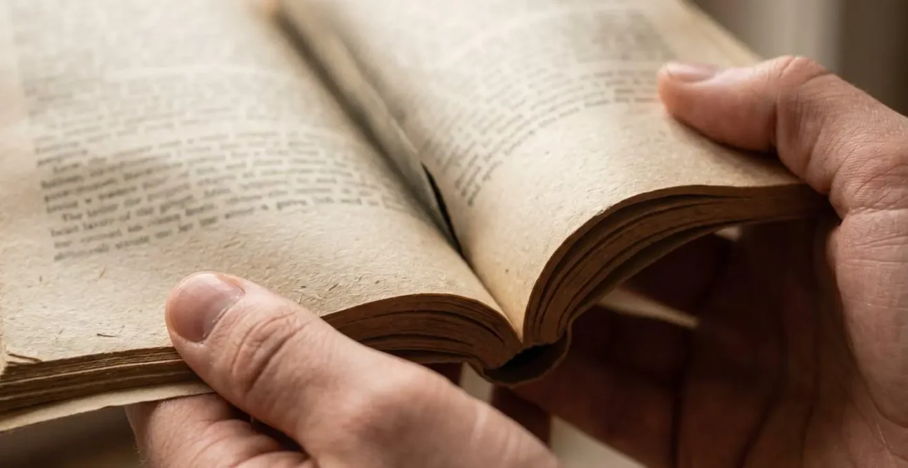 Mani che tengono un libro aperto con luce naturale che illumina le pagine