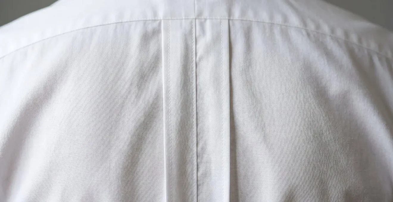 Vista posteriore di camicia bianca con pinces sartoriali che creano linee verticali snellenti dalla spalla alla vita