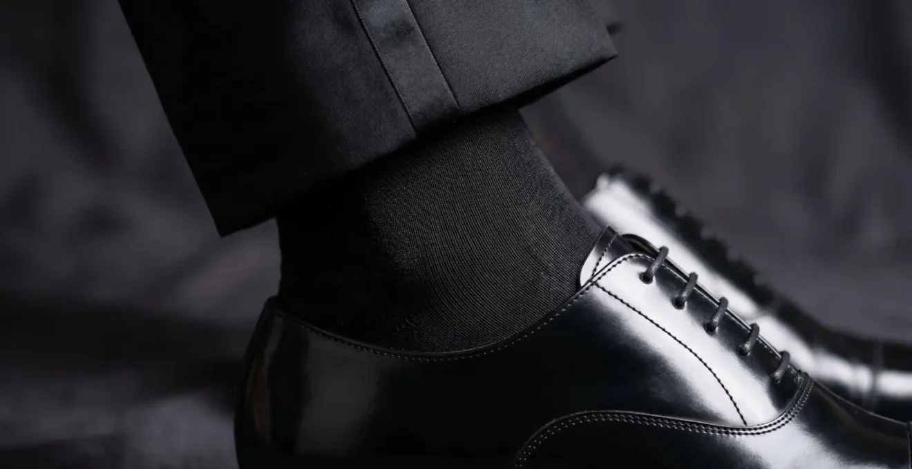 Dettaglio ravvicinato di calzini lunghi in seta nera con scarpe Oxford lucide